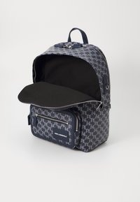 Mochila com padrão azul marinho, com um bolso frontal com fecho, um interior espaçoso e uma pega superior. Apresenta um logótipo em contraste na parte da frente.