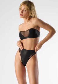 Ensemble de bikini noir comprenant un haut sans bretelles en mesh transparent avec des bonnets structurés et un bas taille haute, échancré avec des détails en mesh.