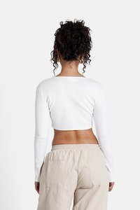Witte cropped long-sleeve top met een ronde halslijn. Draagt een beige broek met een elastische tailleband en twee achterzakken.