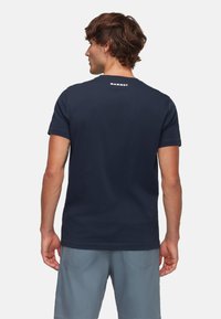 Navyblauw katoenen t-shirt met korte mouwen en een ronde hals, met een wit "Mammut" logo op de achterkant van de hals. Glad textuur.