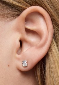 Pendientes de plata en forma de oso, con una superficie texturizada blanca y brillante. Llevados en una oreja perforada, vista en primer plano.