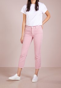 Jeans cropped rosa chiaro con una silhouette aderente, abbinati a una t-shirt bianca a maniche corte e sneakers bianche. Texture denim liscia.