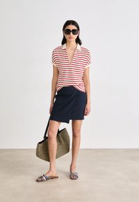 Red and white striped short-sleeve top, navy wrap skirt, large textured black-and-gold bag, blue sandals with decorative buckles.