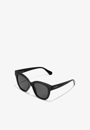 Lunettes de soleil noires en forme d'œil de chat avec des verres sombres et une monture en plastique lisse. Caractéristiques des branches effilées avec texte de logo, fabriquées en Espagne.