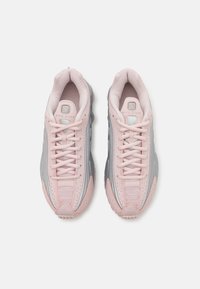 Zapatillas deportivas en rosa y gris con parte superior de malla, patrones texturizados y suela de goma en contraste. Presentan cordones planos y cuello acolchado.