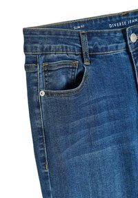 Wąskie dżinsy w ciemnoniebieskim kolorze, z klasycznym pięciopiętrowym wzorem, lekką teksturą i kontrastującymi żółtymi przeszyciami.