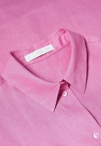 Chemise rose à boutons avec col classique, boutons visibles, et une étiquette de marque blanche à l'intérieur de l'encolure.