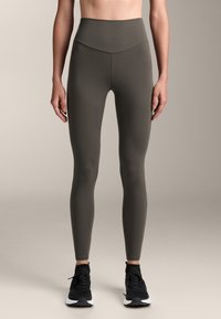 Vysoké legíny tmavě olivové barvy vyrobené z elastického materiálu, se bezešvou konstrukcí, hladkým povrchem a bez viditelných vzorů nebo akcentů.