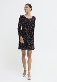 Must mustriga mustreid kaunistatud roosa sädelevaid kive, millel on ümmargune kaelus ja laienev seelik, kantud hõbedaste kõrgete kontsadega kingadega.