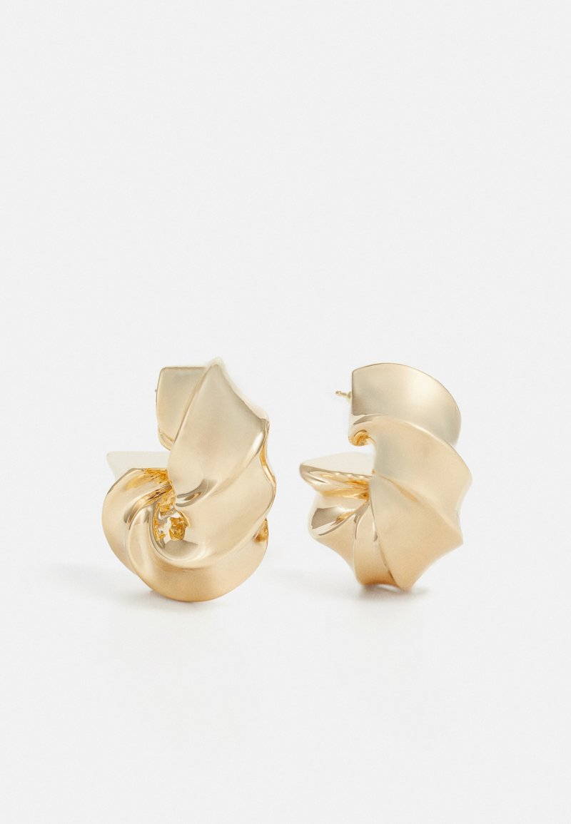 Pendientes de metal dorado texturizado con un diseño escultórico en espiral. Presentan superficies suaves y curvas que reflejan la luz.