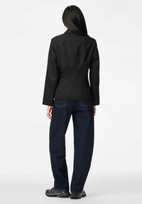 Czarna marynarka w prążki o dopasowanym kroju, zestawiona z luźnymi ciemnymi dżinsami i czarnymi butami sportowymi, widoczna od tyłu.