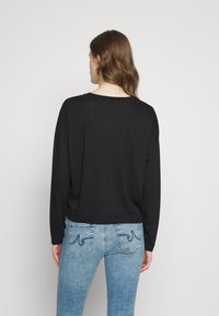 Svart langermet topp med avslappet passform, rund halslinje og senkede skuldre. Kombinert med lys denim jeans med baklommer.