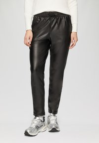 Zwarte neplederen joggingsbroek met een elastische tailleband en koord, met een gladde, glanzende textuur. G gedragen met zilveren sneakers.