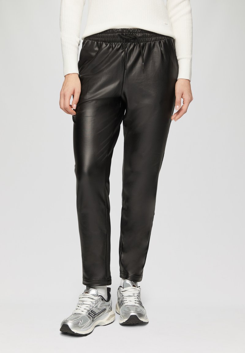 Zwarte neplederen joggingsbroek met een elastische tailleband en koord, met een gladde, glanzende textuur. G gedragen met zilveren sneakers.