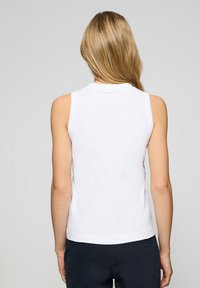 Vit ärmlös topp med rundad krage, mjuk textur, skräddarsydd passform och en fåll som ligger vid midjan. Inga synliga mönster eller accenter.