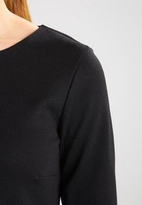 Svart långärmad topp i stretchtyg, med rund halsringning och slät yta, utan synliga mönster eller detaljer i metall.