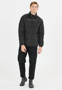 Sort pufferjakke med høj krave og quiltet design. Har lynlåslukning og elastiske manchetter. Stofoverfladen har en mat finish.