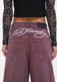 Lila jeans med hög midja, med "Ed Hardy"-logotypen broderad i vitt på bakre midjebandet och två framfickor.