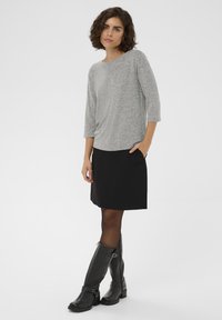 Pelēks, teksturēts garām piedurknēm tops, savienots ar melnu svārku, kuram ir kabatas. Melni ādas zābaki līdz ceļiem ar siksniņas detaļu.