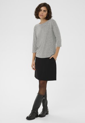 Grå, struktureret bluse med lange ærmer i kombination med en sort nederdel, der har lommer. Sorte læderstøvler til lige under knæet med stropdetalje.