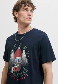Navyblauwe katoenen t-shirt met een grafisch ontwerp van een bebaarde figuur in een zonnebril, met de tekst "MERRY" en "HAPPY HOLIDAYS", omringd door bomen.