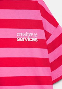 Rot und rosa horizontal gestreifter Stoff mit weißem Text "creative ny services", der auf dem Brustbereich eines Kleidungsstücks gedruckt ist.