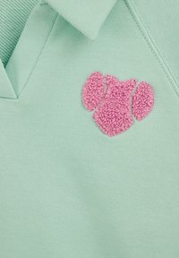 Mintgroene poloshirt met een gestructureerd, roze geborduurd ontwerp dat lijkt op een abstracte vorm. Voorzien van een V-hals en ademende stof.