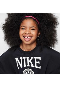 Felpa nera con logo bianco "NIKE", scollatura rotonda e spalle basse. Il modello ha capelli neri ricci e una fascia rosa, con orecchini a cerchio.