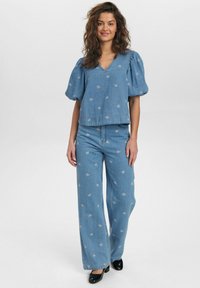 Ljusblå denimblus med puffärmar och blommigt broderi, kombinerad med vida ljusblå denimjeans, bärs tillsammans med svarta klackskor.