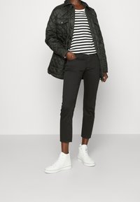 Veste matelassée noire avec un devant boutonné, chemise rayée blanche et noire, et pantalon noir taille courte. Des baskets montantes blanches complètent l'ensemble.