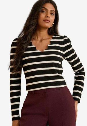 Top a maniche lunghe a righe bianche e nere con scollatura ondulata, abbinato a pantaloni color bordeaux. Realizzato in un tessuto morbido, con taglio aderente.
