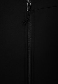 Czarna odzież zapinana na zamek, o gładkiej, matowej fakturze z kontrastowym srebnym zamkiem i detalem ze sznurkiem przy szyi.