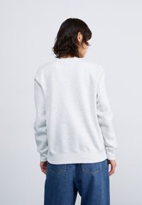 Lichtgrijze sweatshirt met lange mouwen, ronde halslijn, geribbelde manchetten en zoom, gemaakt van een zachte katoenmix, gedragen met blauwe denim broeken.