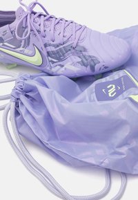 Purple soccer cleats with textured accents and a green swoosh, alongside a matching drawstring bag in lightweight, shiny material.