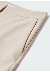 Pantalon beige ajusté avec une poche avant et une boucle de ceinture visible, présenté sur un fond blanc uni.