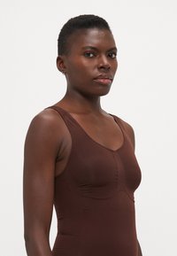 Brown fitted bodysuit with a scoop neckline, thin straps, and textured detailing at the bust. Smooth fabric with a slightly matte finish.