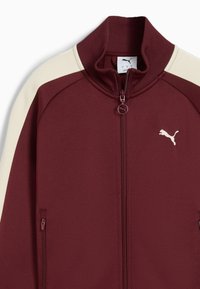 Bordová a krémová zipsová bunda s vysokým golierom, ribbenými manžetami, bočnými vreckami a malým bielym logom Puma na ľavej hrudi. Textúrovaná látka.