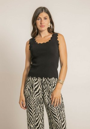 Débardeur noir à côtes avec encolure et ourlet à volants, associé à un pantalon ample en imprimé zèbre noir et crème. Texture douce, coupe ajustée.