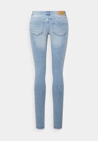 Jeans skinny azul claro com um acabamento desbotado, design de cinco bolsos e um patch de couro na cintura. Apresenta bainhas desfiadas nos punhos.