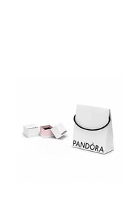 Bolsa de regalo de papel blanco con asas negras, etiquetada "PANDORA". Incluye pequeñas cajas de joyería en blanco y rosa, una de ellas parcialmente abierta.