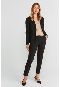 Musta räätälöity bleiseri, beige paita ja mustat slim fit -housut. Materiaalit: kangas, jossa on sileä rakenne. Korostus: terävät mustat kengät.