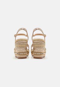 Sandales compensées avec un design en fibres naturelles tissées, des brides synthétiques beige et des accents métalliques. Comprend une bride de cheville et une semelle intermédiaire texturée.