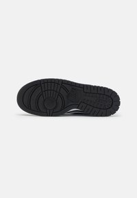 Black sneaker sole with textured rubber, featuring a circular pattern and prominent tread grooves. Nike logo embossed on the side.