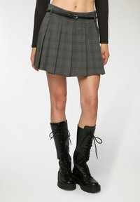 Gonna plissettata grigia a quadri con una cintura nera, abbinata a stivali neri con lacci alti fino al ginocchio e suole spesse.