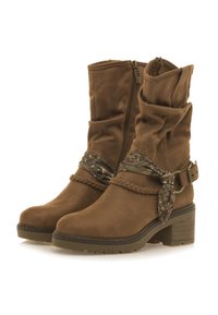 Botines de ante marrón con un diseño arrugado, cremallera lateral, correa trenzada y herrajes decorativos. Presentan un tacón grueso y una suela texturizada.