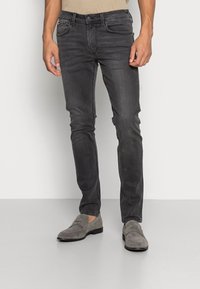 Jeans de mezclilla gris oscuro con un corte ajustado, diseño de cinco bolsillos y un sutil detalle de costura. Combinados con mocasines de ante grises.