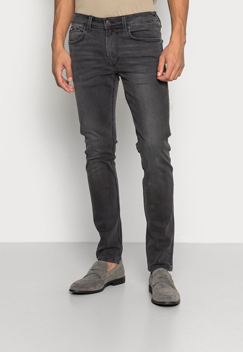 Jeans de mezclilla gris oscuro con un corte ajustado, diseño de cinco bolsillos y un sutil detalle de costura. Combinados con mocasines de ante grises.