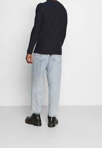 Haut à manches longues bleu marine, jean bleu clair avec poches arrière et bottes noires à lacets. Tissu lisse avec une coupe ajustée aux épaules.