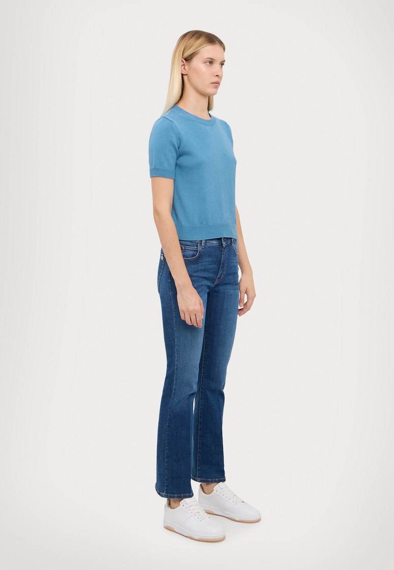 Lyseblå kortermet genser med rund hals, kombinert med blå utsvingte jeans og hvite joggesko. Enkel, uformell antrekk.