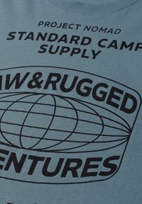 Tissu bleu avec texte noir indiquant « Project Nomad Standard Camp Supply Raw & Rugged Adventures » et un dessin au trait d'un globe.